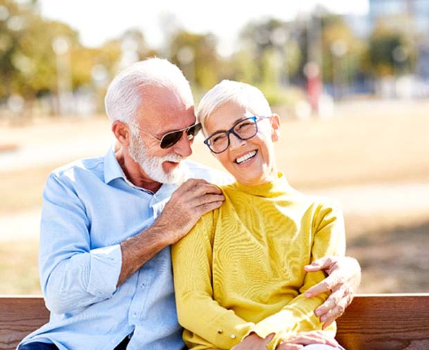 Mature couple smiling while sitting on bench outside