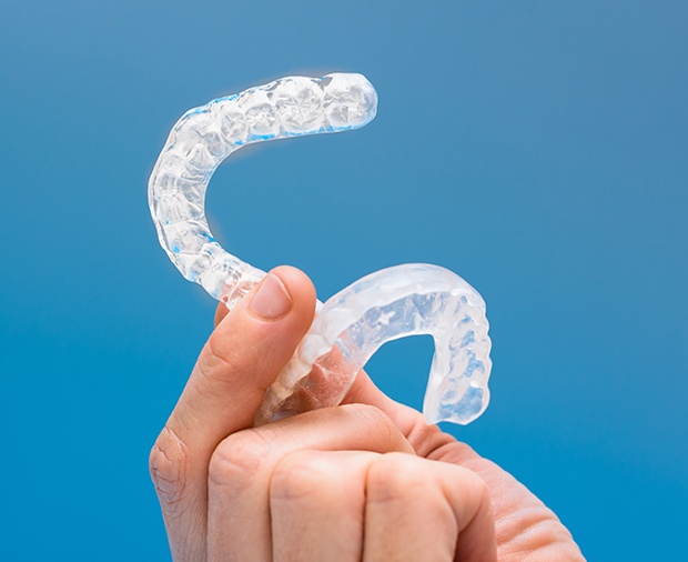 Hand holding set of clear nightguards for bruxism