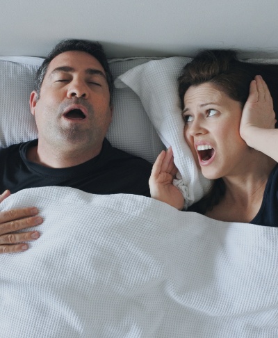 Frustrated woman next to man in need of sleep apnea therapy