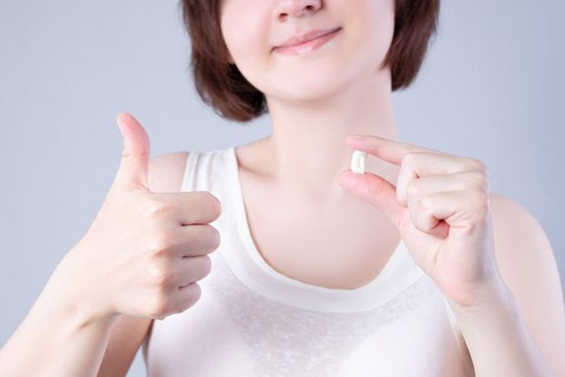 Woman holding her extracted tooth, making thumbs-up gesture