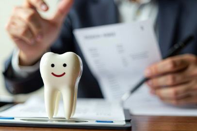 Tooth model with smiley face on it in front of man doing paperwork