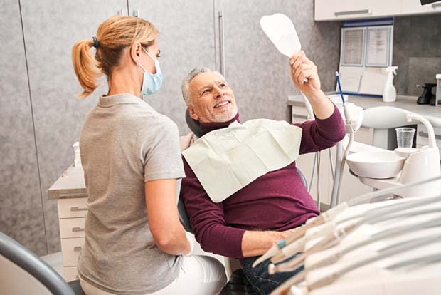 Man with dentures in Bedford smiling in dentist's mirror