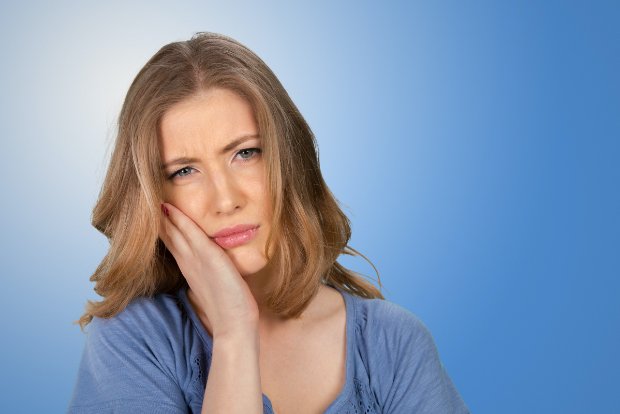 Woman in need of emergency dentistry holding cheek in pain