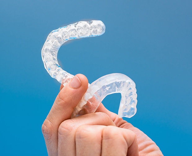 Hand holding set of clear nightguards for bruxism