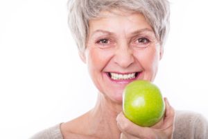 Woman holding apple after transitioning to dental implants