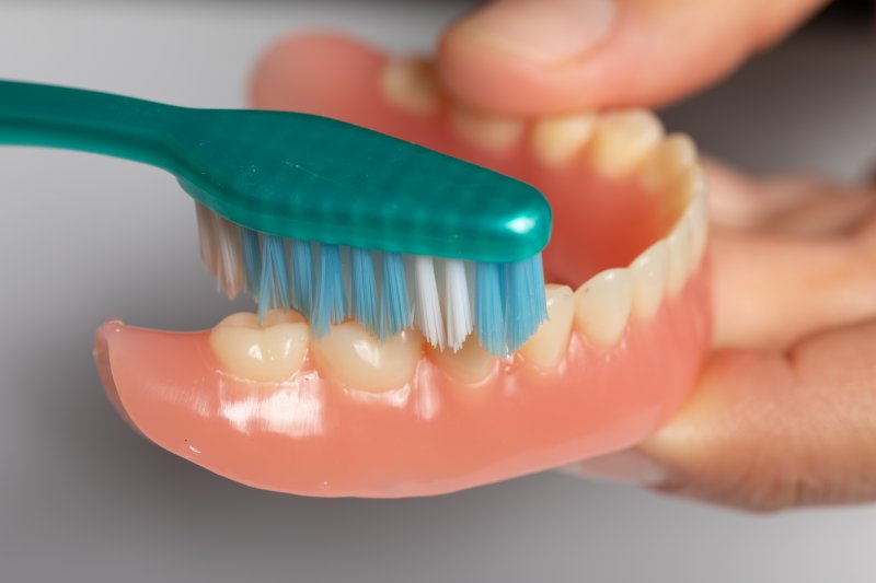 person caring for dentures by brushing them